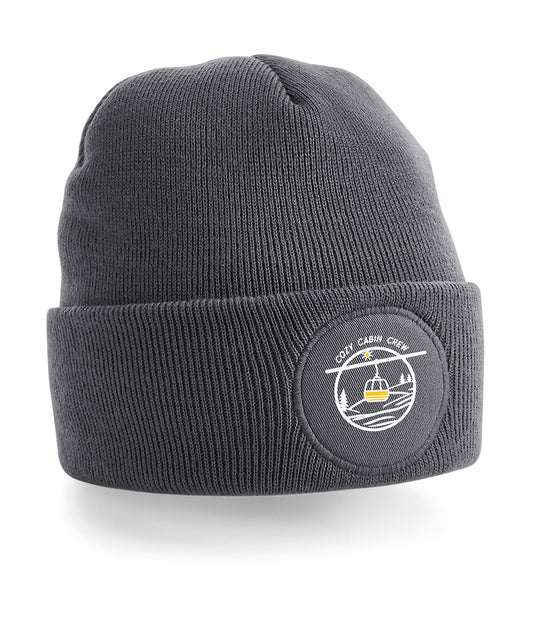 Beanie of muts met Logo van een gele eitjes lift in de bergen met als bijschrift “cozy cabin crew” ludieke afbeelding voor de gezellige skier of snowboarder